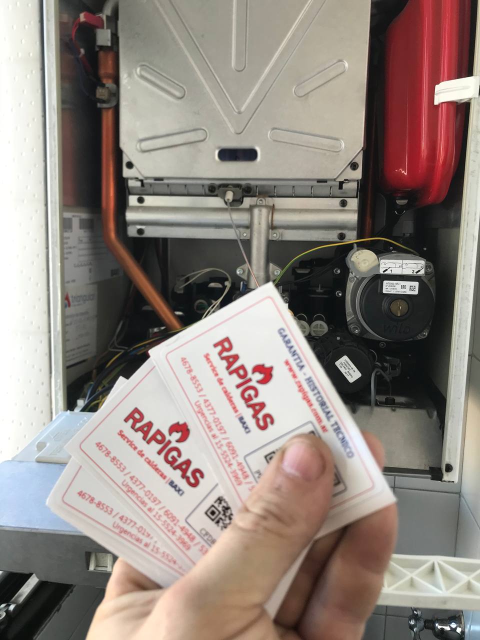 Técnico de RAPIGAS con tarjetas de servicio frente a una caldera BAXI
